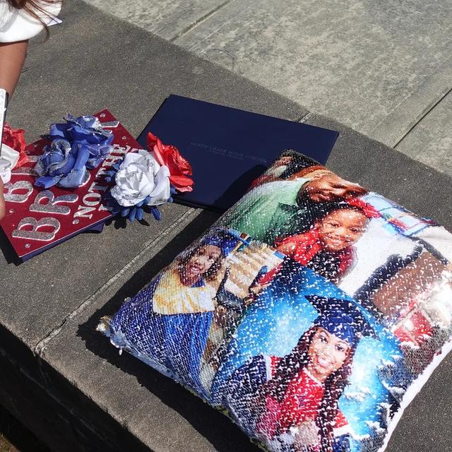 Qstomize.com - Personalize Your Pillow with Custom Reversible Sequin Design Vibrant graduation celebration with decorative pillow, flowers, and navy cap against a textured backdrop.