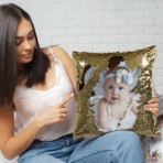 Qstomize.com - Personalize Your Pillow with Custom Reversible Sequin Design Young woman points at a glamorous baby portrait pillow, adding style to her cozy space.